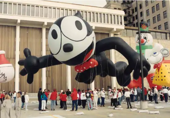 Mickey Mouse balloon from a parade, surrounded by a crowd in a city square.