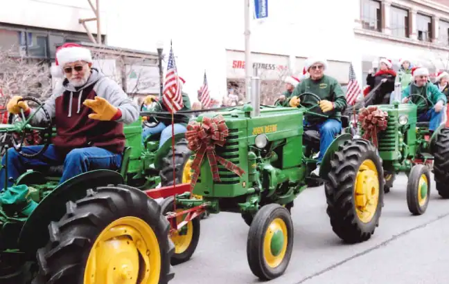 Group of people riding decorated tractors in a holiday parade, celebrating community and culture.