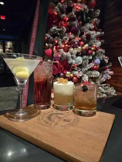 Assorted cocktails on a wooden board with a decorated Christmas tree in the background.