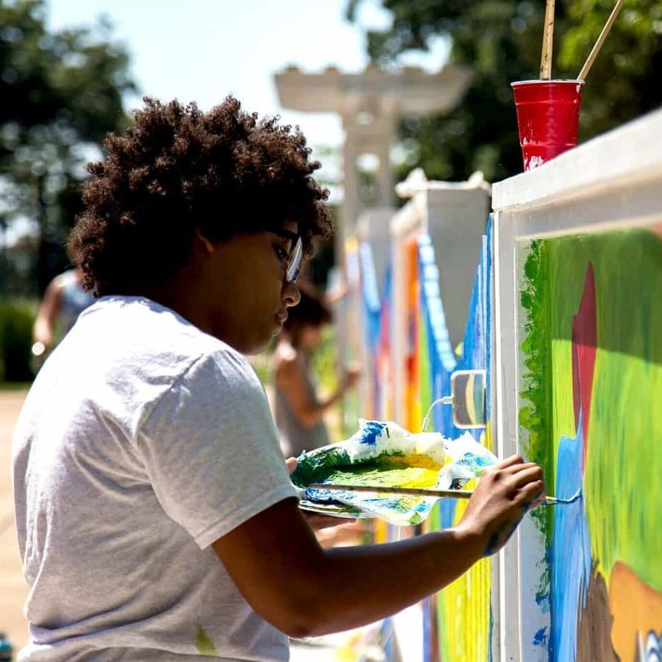Young artist painting colorful mural at outdoor cultural event.