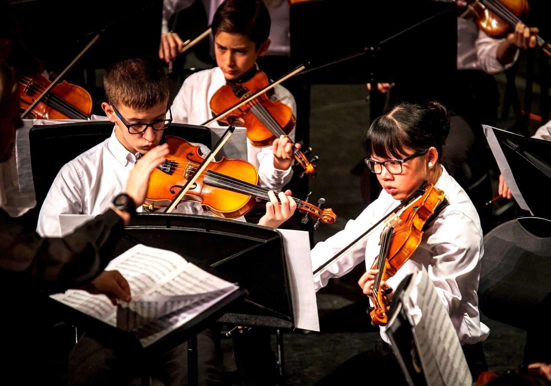 Young musicians playing violins during a classical concert.