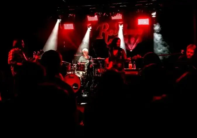 Live band performing on stage with drums, guitar, and keyboard in a vibrant concert setting.